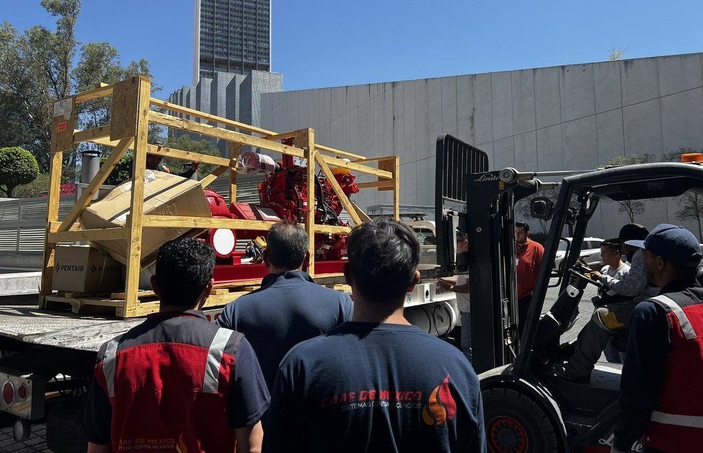 Pumping equipment being unloaded with a forklift while personnel look on.