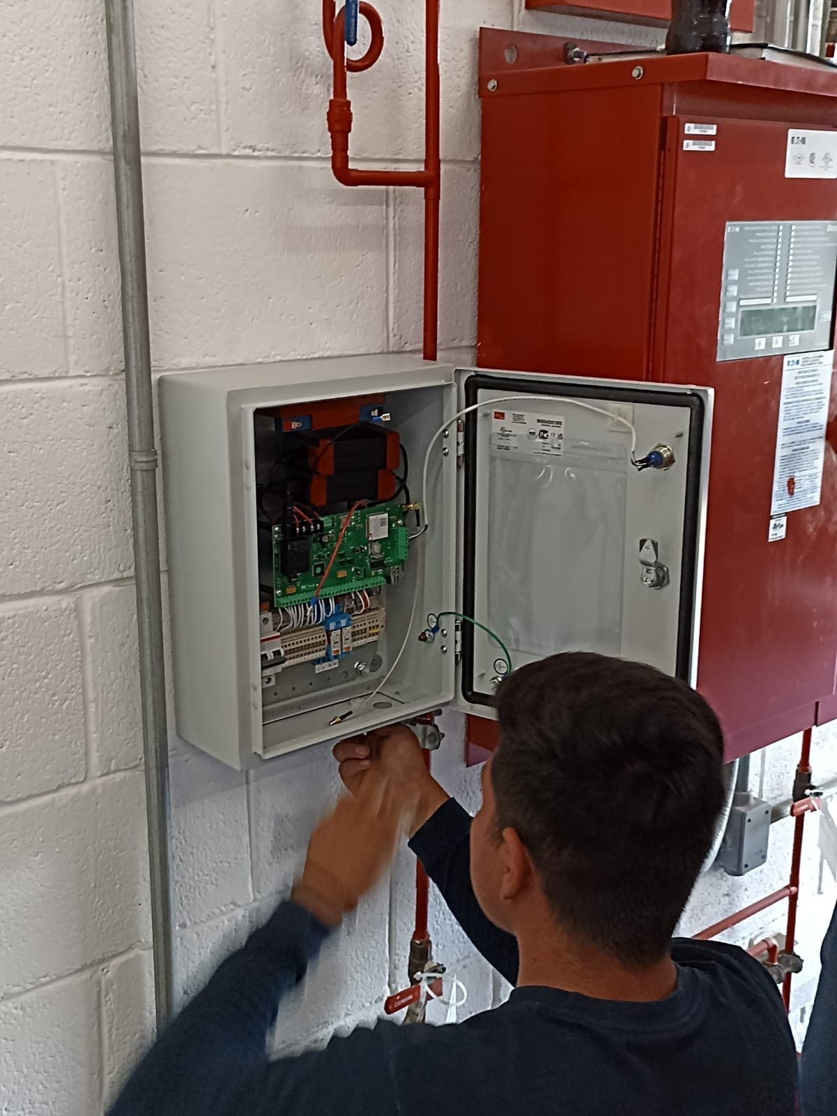 A technician checks the wiring inside the monitoring unit cabinet, next to a fire pump controller.