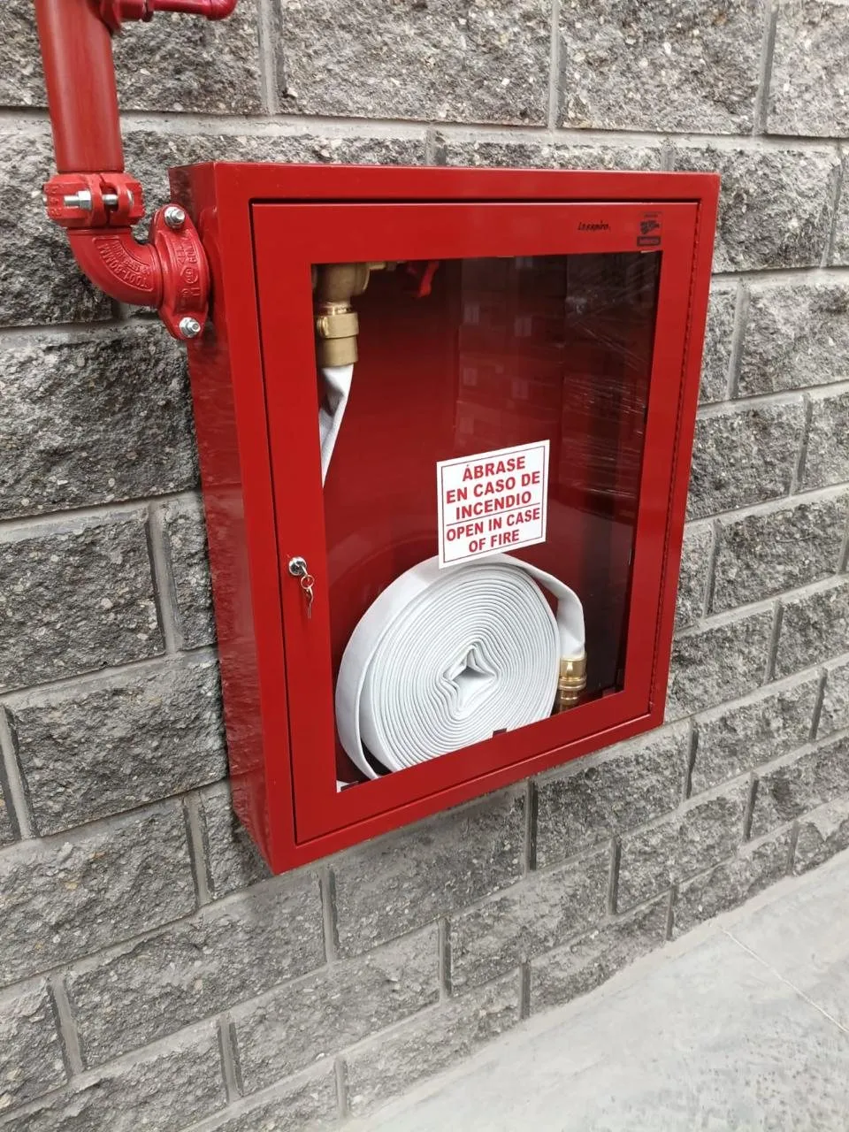 Red hose cabinet with hose and valve, mounted on a concrete block wall.