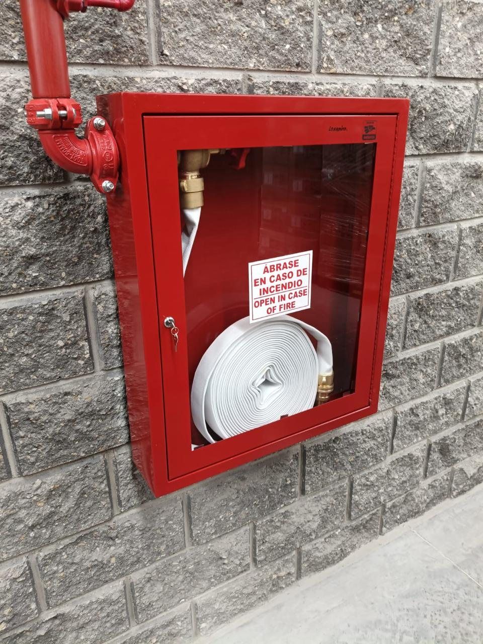 Red hose cabinet with hose and valve, mounted on a concrete block wall.