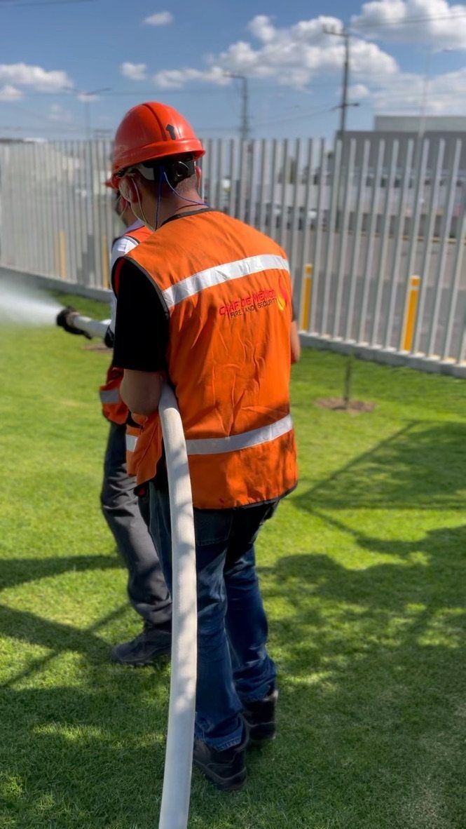 Práctica de brigada: personal con casco y chaleco de CAAF de México maneja una manguera con descarga de agua.