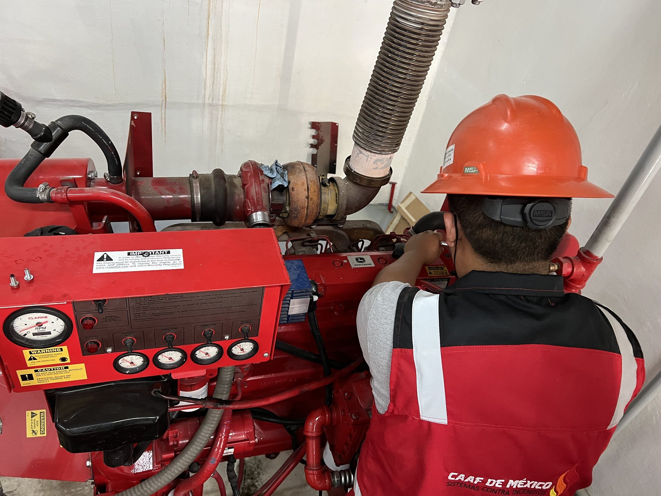 A CAAF de México technician in an orange hard hat works on the Clarke diesel engine of a fire pump; in the foreground, the engine's instrument panel.