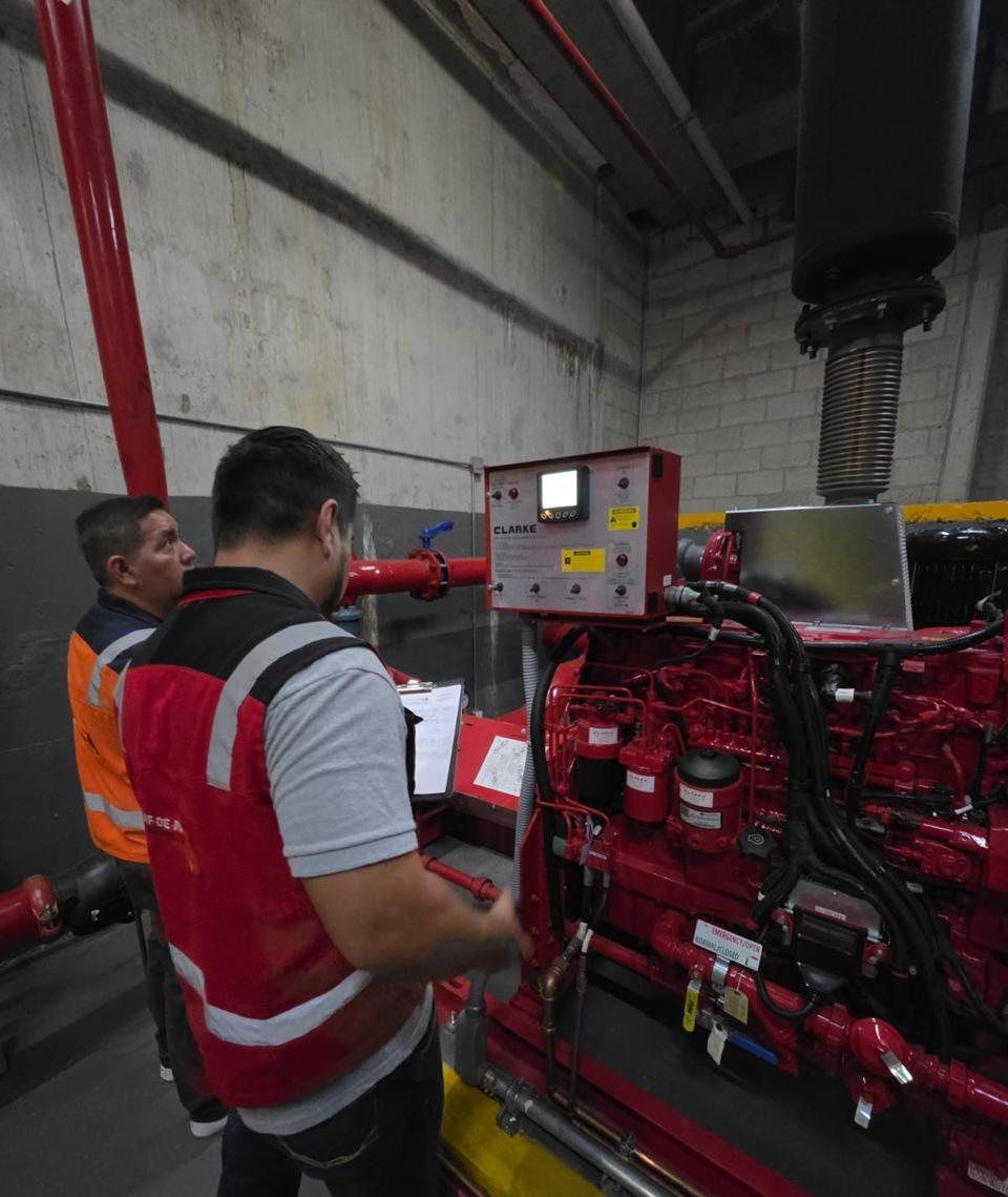 Two technicians inspect the diesel engine of a fire pump inside the fire pump room.