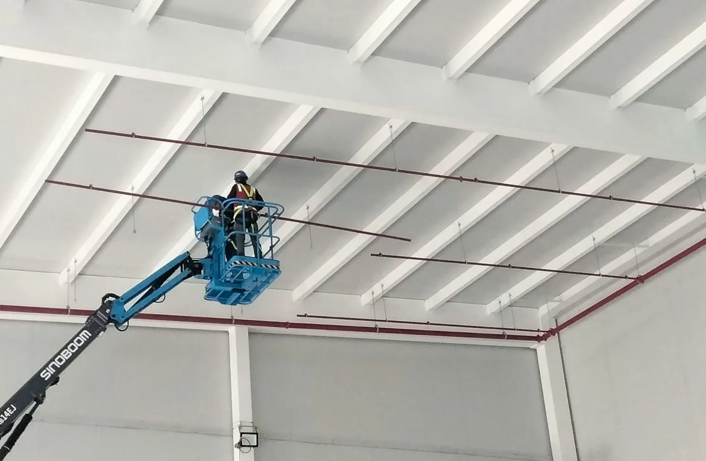 Technician on an aerial lift installs the sprinkler piping at ceiling level.