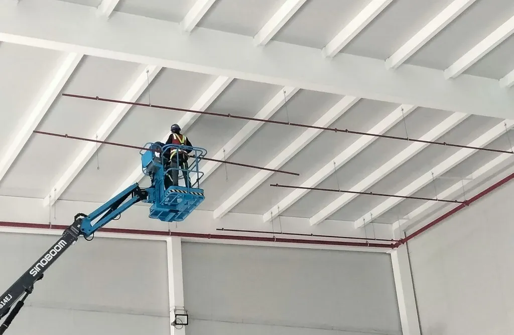 Technician on an aerial lift installs the sprinkler piping at ceiling level.