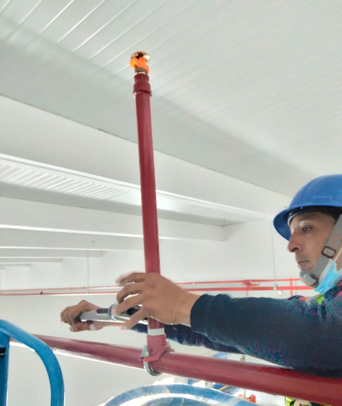 Technician on an aerial lift works on a vertical section of piping with a sprinkler at the end.