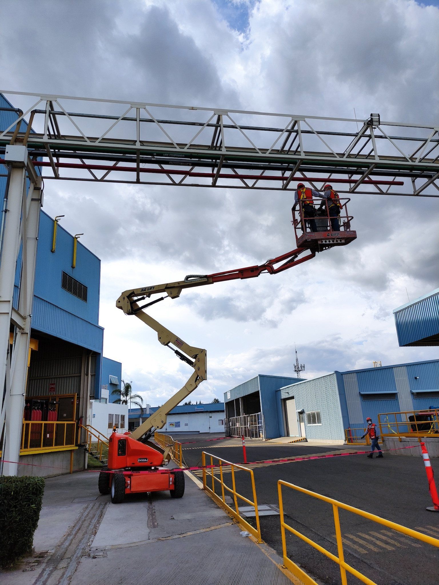 Articulating boom lift carries two technicians up to an outdoor pipe rack at a plant.