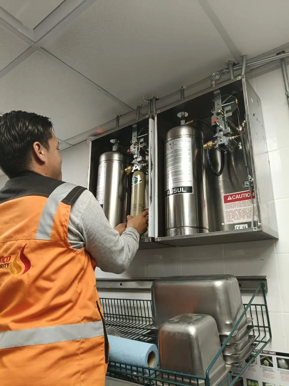 Technician checks the open enclosure of an Ansul system with two agent tanks, in an industrial kitchen.